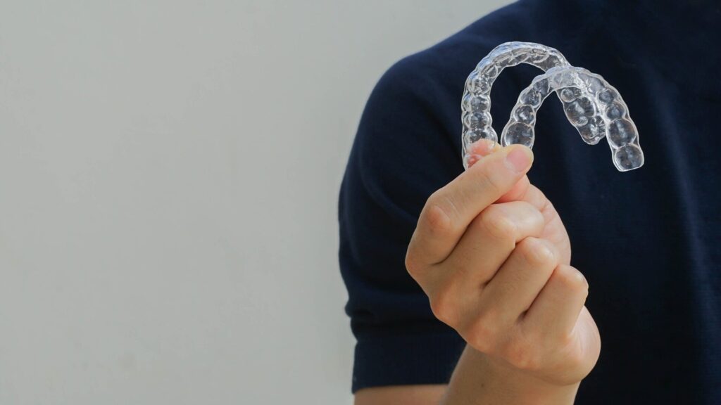 close up man hand holding dental aligner retainer (invisible) on background for beautiful teeth treatment course concept